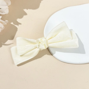 Detail of cream velvet bow hair clip with rose flower ornament on a neutral tray
