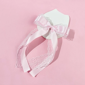 Close-up of sweet pink satin bow hair clip with white lace trim and long streamers