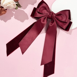 Détail du nœud papillon en velours et satin bordeaux avec longs rubans sur fond rose