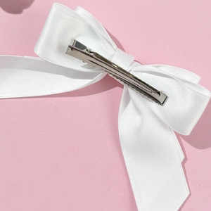 Vue détaillée de la pince à cheveux en satin blanc avec fermoir en métal sur fond rose