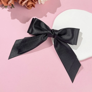 Gros plan d'une pince à cheveux en satin noir avec double nœud sur un fond rose élégant