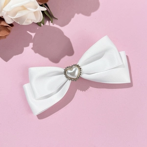 Eleganter weißer Satin-Bogen-Haarclip mit Herzperle und Strass auf rosa Hintergrund