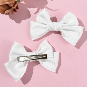 Détail de barrettes à nœud blanc en satin avec bordure ondulée et pince en métal