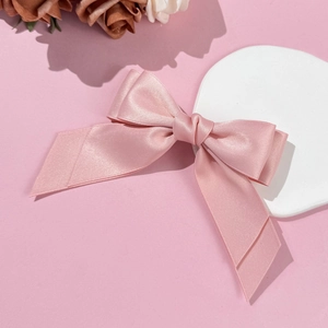 Détail de la pince à cheveux en satin rose à double nœud sur un présentoir décoratif