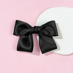 Detailed macro view of a black satin bow hairclip showing fine silk fabric texture