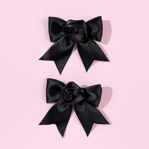 Close-up of black satin bow hair clips with central fabric roses on pink background