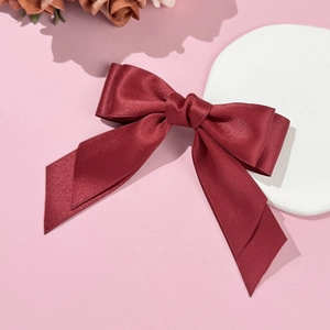 Détail de la pince à cheveux double nœud en satin bordeaux sur fond rose pastel