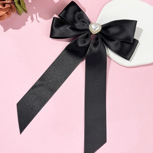 Détail d'un nœud en satin noir avec perle cœur en strass sur un fond rose doux