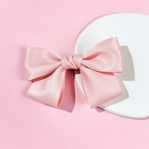 Elegant light pink satin bow hair clip on a minimalist white stone display stand