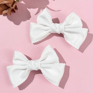Détail de barrettes nœuds blancs en satin avec bords dentelés sur fond rose