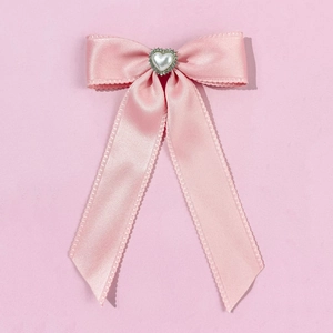 Vue détaillée du nœud en satin rose avec perle en cœur et strass sur la barrette
