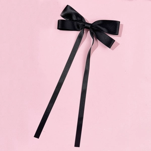Detail of elegant black satin ribbon bow hair clip with long streamers on pink background