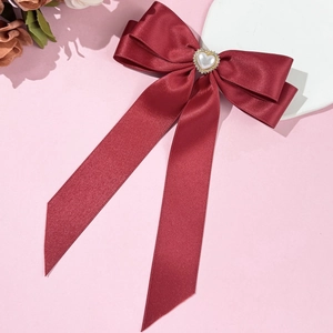 Détail d'une barrette à nœud en satin bordeaux avec cœur en perle et strass élégant