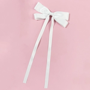Detail of elegant white satin ribbon bow hair clip with long streamers on pink background