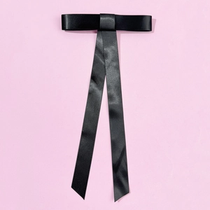 Détail d'une élégante pince à cheveux en satin noir avec de longs rubans sur fond rose