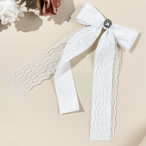 Detailed view of white eyelash lace bow hairclip with rhinestone center and long ribbon