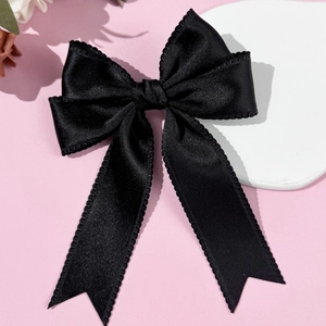 Detail of elegant black satin bow hair clip with decorative lace trim on pink surface