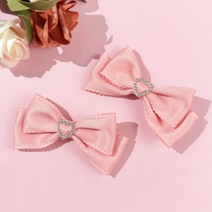 Nahaufnahme der rosa Satin-Bogen-Haarspangen mit herzförmigen Strasssteinen im Set