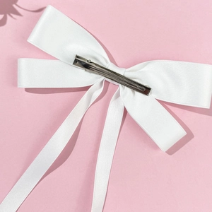 Elegant white satin oversized bow hair clip with silver metal clip on pink background