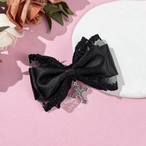 Detail of Gothic black lace bow hair clip with vintage silver cross pendant on pink background