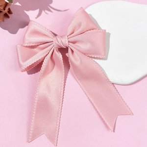 Detailed close-up of pink satin bow hair clip with long ribbon tails and scallop edges