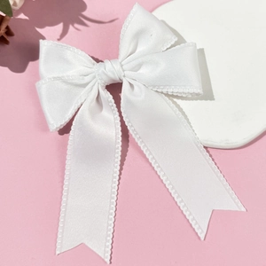Detail of white satin ribbon bow with intricate scalloped lace edges on a pink background