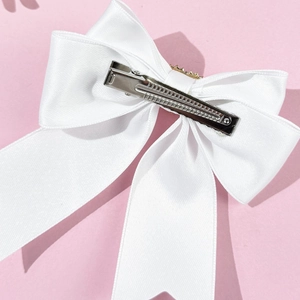 Detailed view of white satin bow hair clip with gold crown on pink background