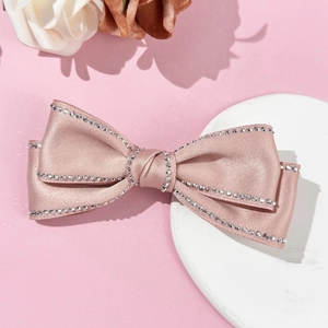 Détail d'une pince à cheveux nœud en satin rose avec strass argentés et tissu soyeux