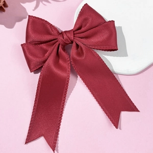 Detail of burgundy satin bow hair clip with wavy scalloped edges and long ribbons