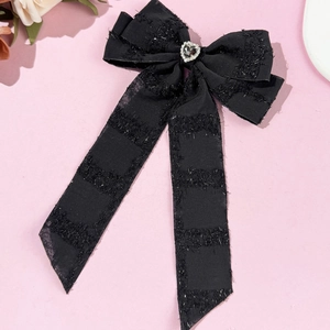 Detail of black bow hair clip with rhinestone heart and long streamers on pink surface