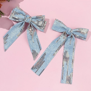 Close-up of light blue denim bow hair clip with sparkling sequins and long ribbons