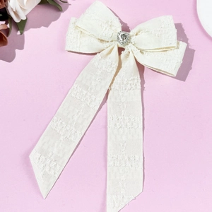 Detailed view of cream tweed bow hair clip with rhinestone heart and long ribbons