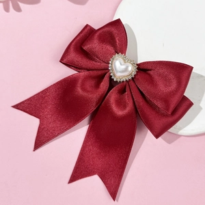 Macro detail of dark red satin bow hair clip with heart-shaped pearl and rhinestones