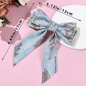 Detail of light blue denim bow hair clip with bronze sequins and long ribbon streamers