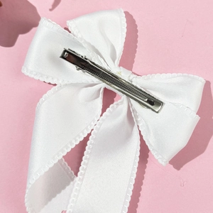 Elegant white satin ribbon bow hair clip with lace edges on a soft pink background