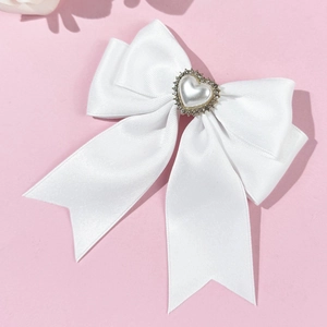 Detail of white satin bow hairclip featuring a heart pearl with rhinestone metal frame