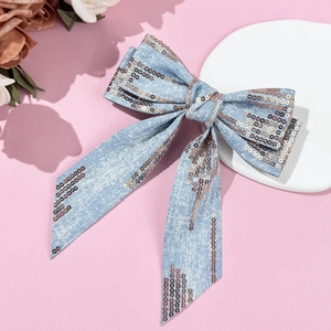 Detailed view of denim bow hair clip with bronze sequins on a soft pink background