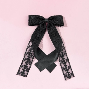 Elegant black lace bow hair clip with long ribbon streamers on a pink background