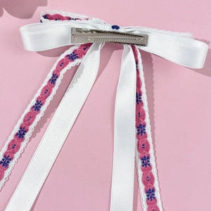 Detail of white satin bow hair clip with floral embroidery and silver metal alligator clip