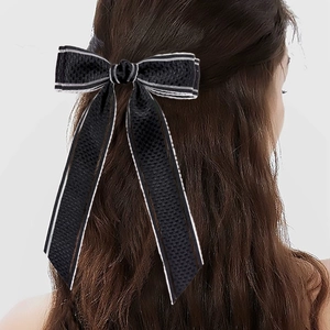 Détail d'une barrette à nœud noir avec rayures blanches sur des cheveux foncés