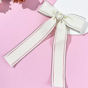 Detail of checkered cream bow hair clip with pink stripes and black wavy lace edges