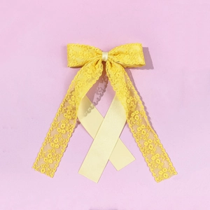 Detail of yellow lace bow hair clip with elegant floral texture and long silk streamers