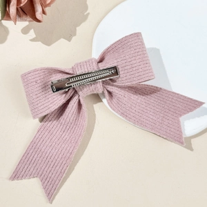 Elegant pink knit bow hair clip with silver duckbill metal grip on a white plate