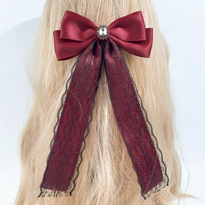 Detail of burgundy satin bow hair clip with crystal center and lace ribbons on blonde hair