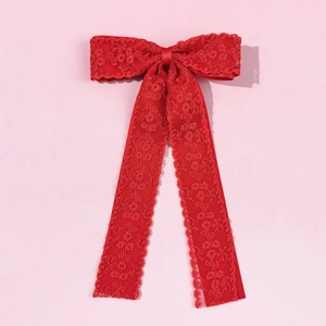 Close-up of elegant red lace bow hair clip with long ribbons on pink textured background