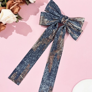 Detailed view of oversized denim bow hair clip with rose gold sequins on pink background