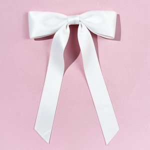 Dettaglio del fermaglio per capelli con fiocco di raso bianco su sfondo rosa