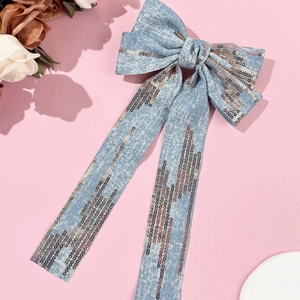 Detail of light blue denim hair clip with bronze sequins and long ribbon streamers