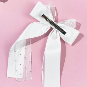 Détail d'une pince à cheveux à double nœud en tulle blanc et ruban satin sur fond rose