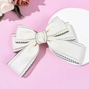 Detail of cream-white bow hair clip featuring checkered jacquard fabric and black scalloped edges